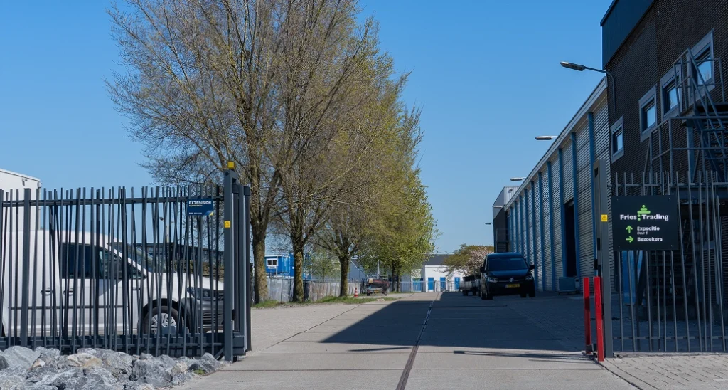 Geopende toegang naast het bedrijfspand met hekwerk en poortkolommen